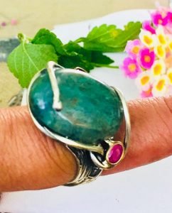 oval cabochon ring in a finger surrounded by leaves and flowers