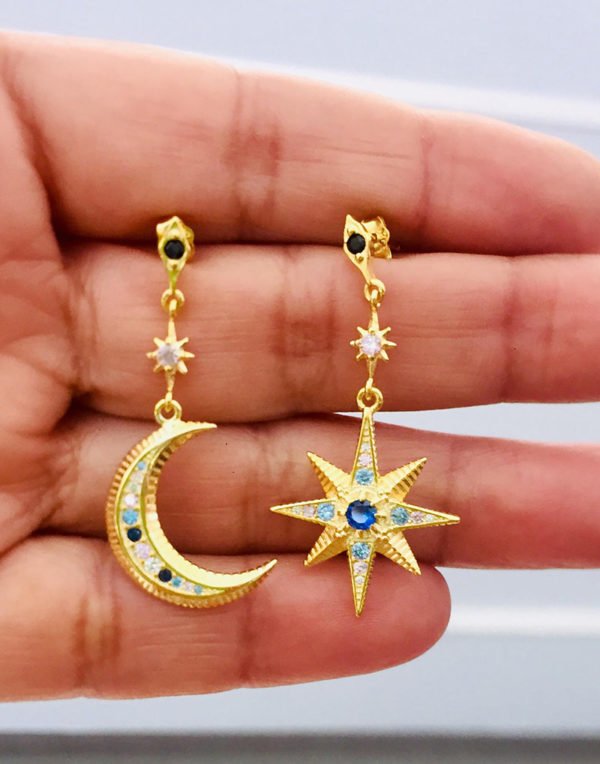 gold colored moon star form earrings appearing on a woman's hand